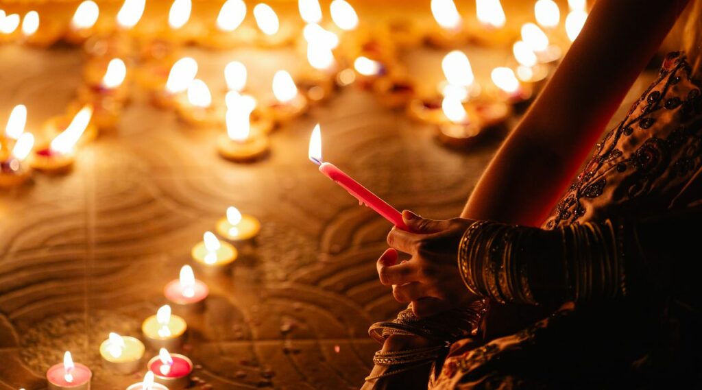 A close-up of hands holding a candle during a Diwali festival, surrounded by glowing candles.